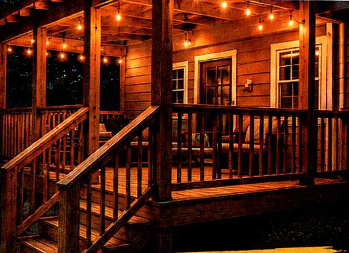 Covered wooden porch and stairs lit with string lights at dusk
